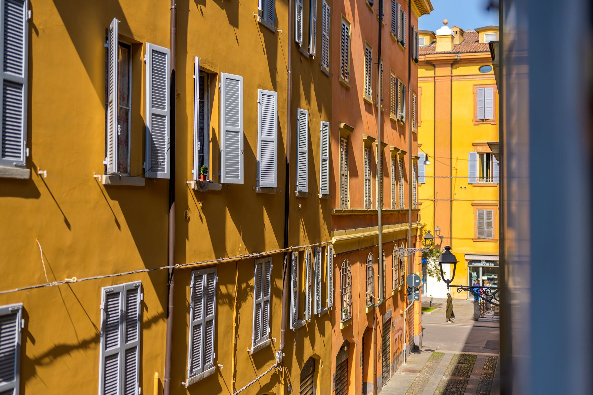 La via vista da una finestra dell'appartamento, con le case gialle e arancio e le persiane