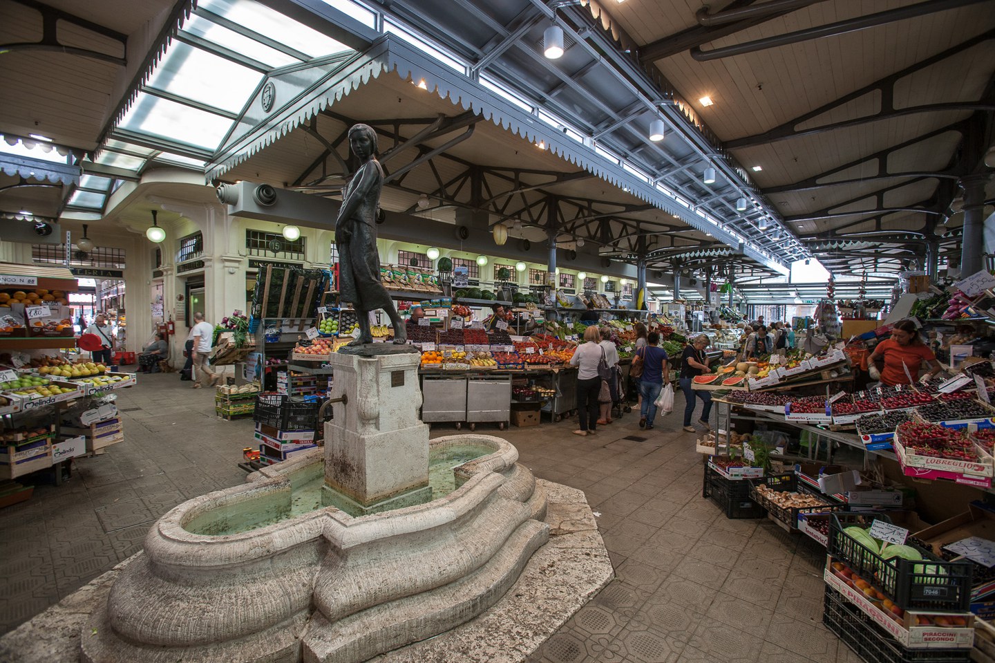 Inside the Albinelli Market in Modena: the fountain statue and the fruit and vegetable stalls under the iron roof