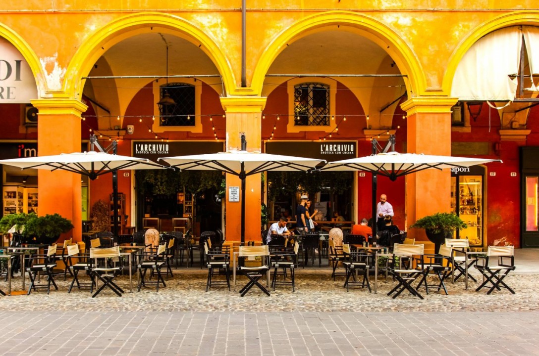 The outdoor tables of Bar Archivio in Modena: white umbrellas and tables under the orange arcades