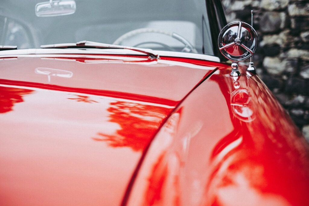 The red bonnet of a vintage car with its chrome ornament